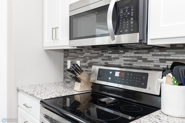 kitchen with white cabinetry, stainless steel appliances, light stone countertops, and backsplash