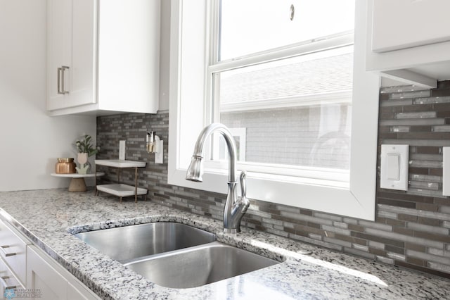 room details featuring white cabinetry, decorative backsplash, light stone counters, and a sink