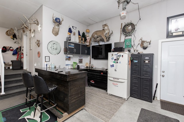 kitchen featuring freestanding refrigerator, dark cabinets, dark countertops, and concrete floors
