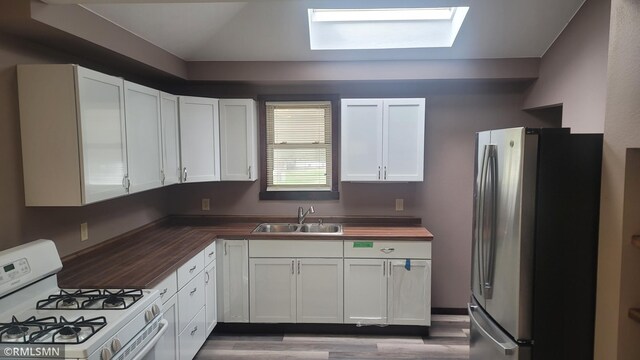 kitchen with freestanding refrigerator, white gas range, white cabinets, a sink, and wood counters