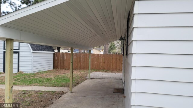 view of patio / terrace featuring fence, a storage unit, an outbuilding, and a carport