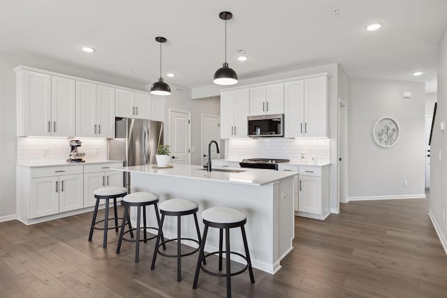 kitchen featuring stainless steel appliances, a sink, backsplash, dark wood finished floors, and recessed lighting