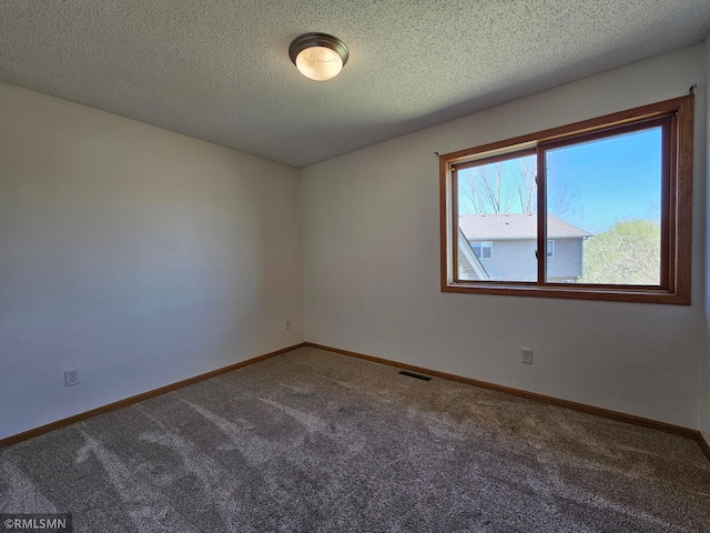 empty room with carpet flooring, a textured ceiling, visible vents, and baseboards