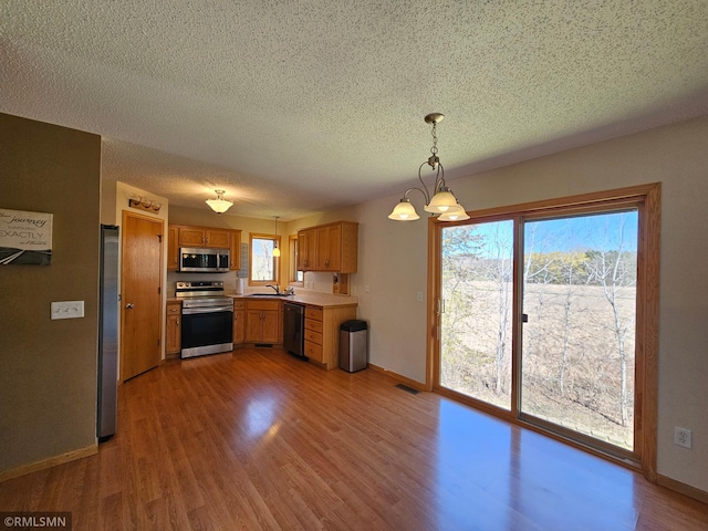 kitchen with a textured ceiling, light wood-type flooring, a sink, baseboards, and stainless steel appliances