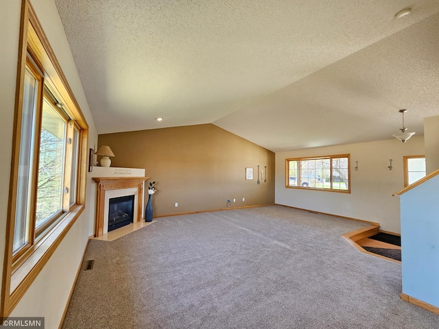 unfurnished living room with carpet floors, visible vents, baseboards, a fireplace with flush hearth, and vaulted ceiling