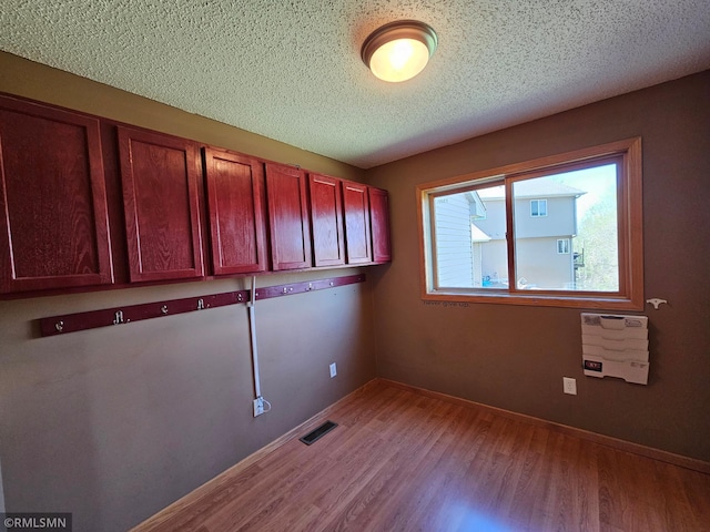 washroom with light wood-style floors, baseboards, a textured ceiling, and visible vents