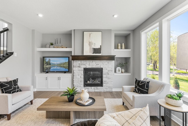 living area with wood finished floors, a stone fireplace, stairs, recessed lighting, and baseboards