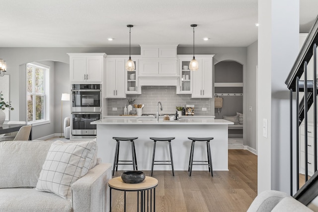 kitchen with arched walkways, double oven, tasteful backsplash, light countertops, and light wood-type flooring