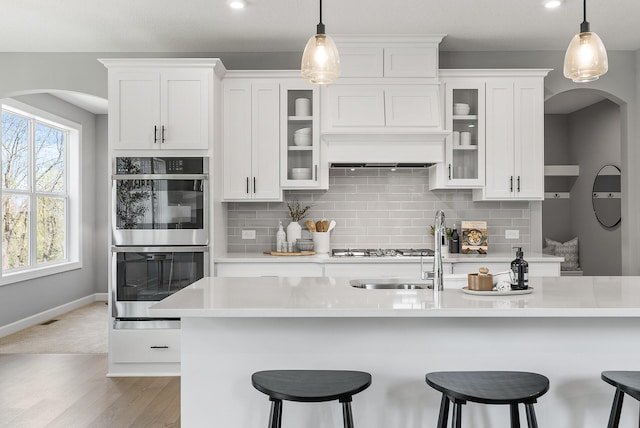 kitchen featuring double oven, arched walkways, a breakfast bar area, decorative backsplash, and recessed lighting