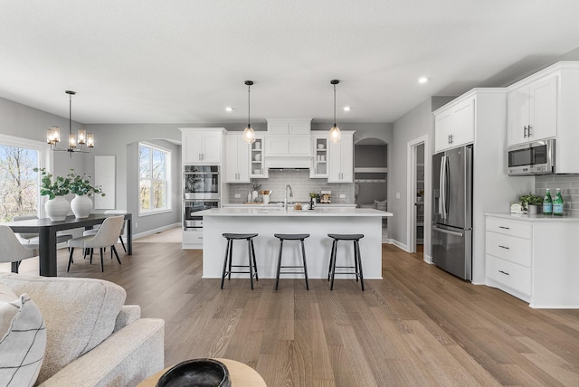 kitchen featuring stainless steel appliances, arched walkways, a kitchen breakfast bar, decorative backsplash, and glass insert cabinets