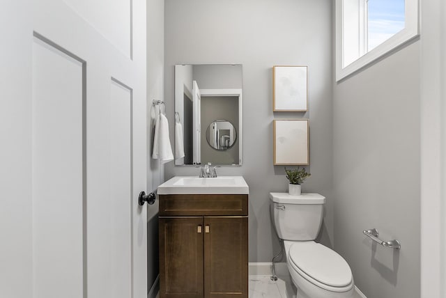 half bathroom featuring marble look tile flooring, toilet, baseboards, and vanity