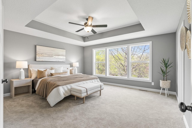 carpeted bedroom featuring a tray ceiling, baseboards, ceiling fan, and a textured ceiling