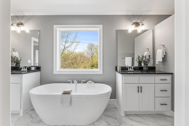 bathroom with marble finish floors, a soaking tub, two vanities, and baseboards