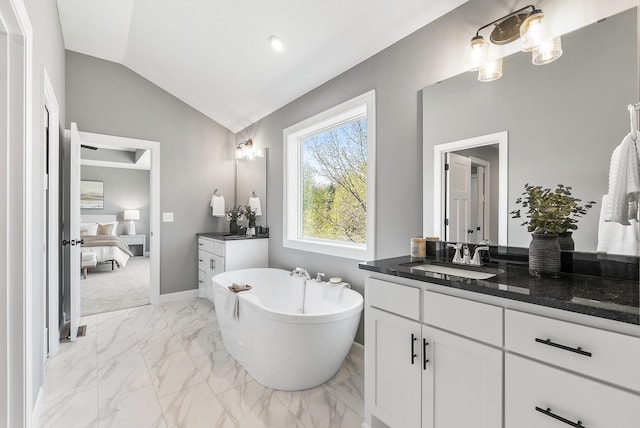 ensuite bathroom featuring marble look tile flooring, lofted ceiling, a soaking tub, vanity, and baseboards