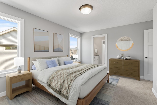 bedroom featuring baseboards, light colored carpet, and connected bathroom