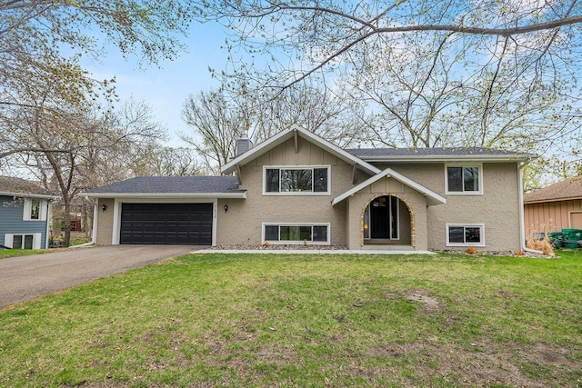 split foyer home with aphalt driveway, an attached garage, stucco siding, a front lawn, and a chimney