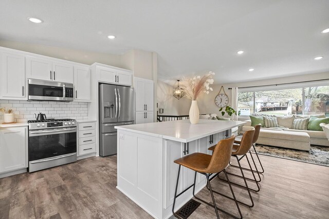 kitchen featuring a kitchen breakfast bar, stainless steel appliances, white cabinets, and wood finished floors
