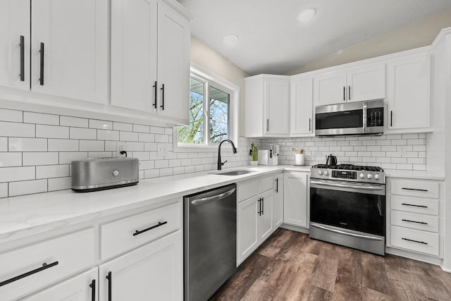 kitchen with vaulted ceiling, a sink, white cabinetry, dark wood-type flooring, and stainless steel appliances