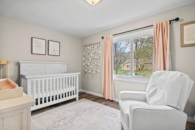 bedroom featuring a nursery area, wood finished floors, and baseboards