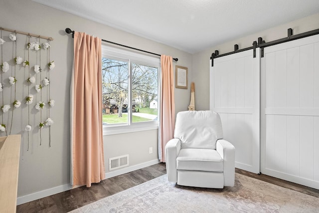 living area featuring a barn door, visible vents, wood finished floors, and baseboards