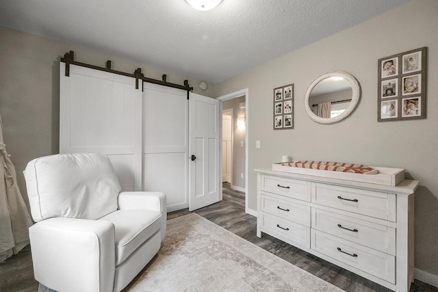 living area featuring a textured ceiling, a barn door, baseboards, and dark wood finished floors