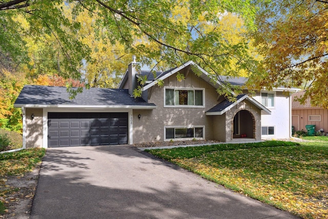 split level home with aphalt driveway, an attached garage, stucco siding, a front lawn, and a chimney