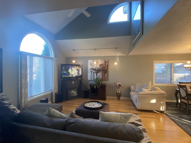 living room with vaulted ceiling, plenty of natural light, wood finished floors, and ceiling fan with notable chandelier