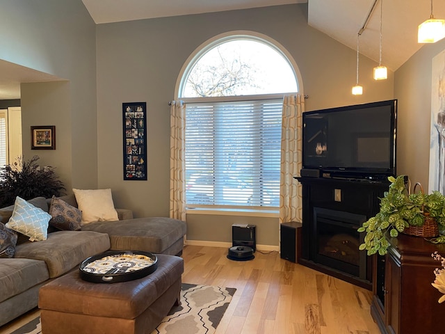 living area with light wood-type flooring, baseboards, high vaulted ceiling, and a fireplace