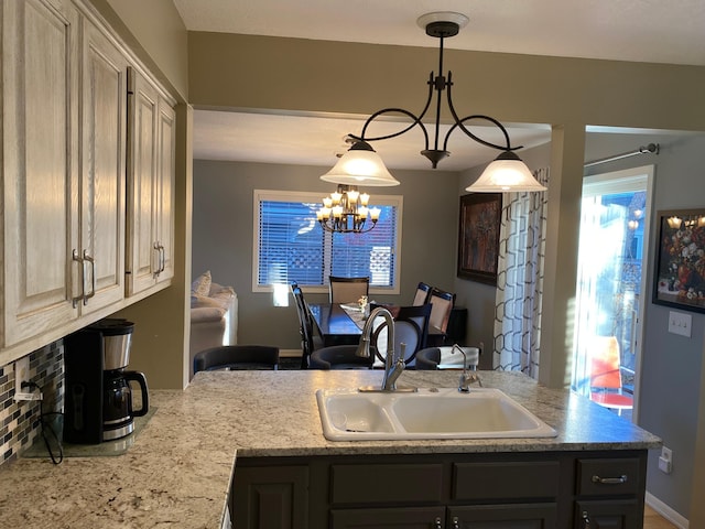 kitchen featuring light stone counters, a sink, decorative light fixtures, and an inviting chandelier