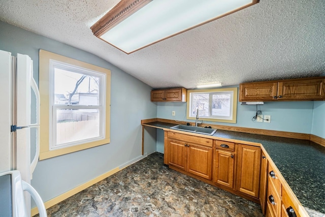 kitchen featuring a sink, brown cabinetry, vaulted ceiling, and a textured ceiling