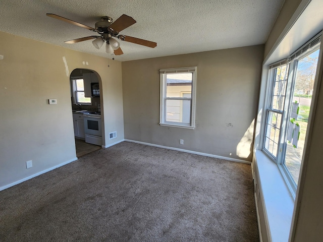 empty room featuring arched walkways, plenty of natural light, a ceiling fan, and carpet floors