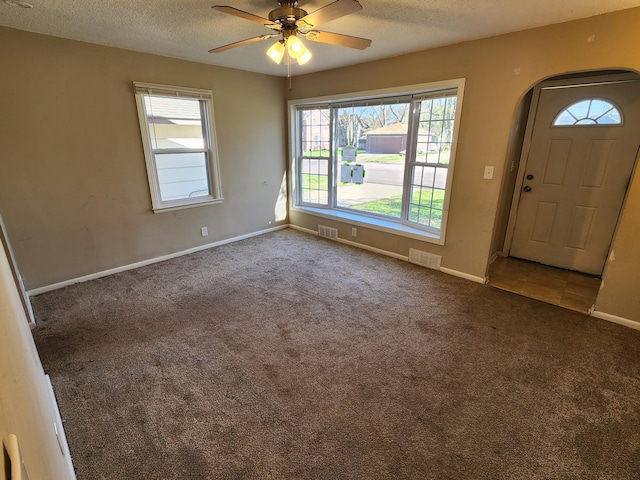 carpeted foyer with arched walkways, a textured ceiling, and visible vents