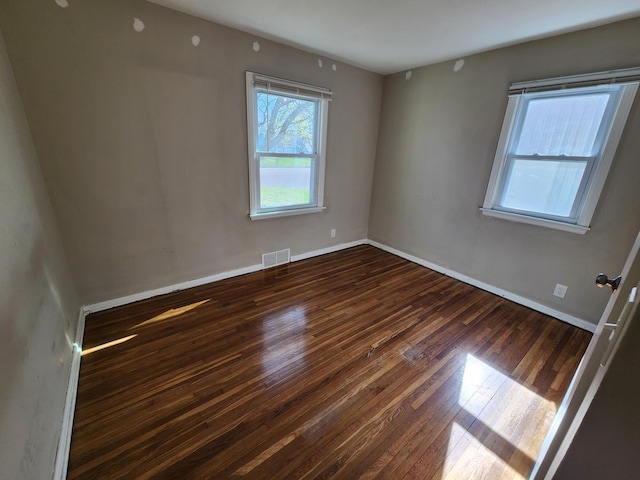 empty room featuring visible vents, wood-type flooring, and baseboards