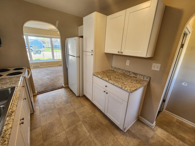 kitchen featuring range with electric stovetop, arched walkways, baseboards, freestanding refrigerator, and white cabinetry