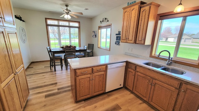 kitchen with brown cabinets, a sink, dishwasher, a peninsula, and light wood-type flooring