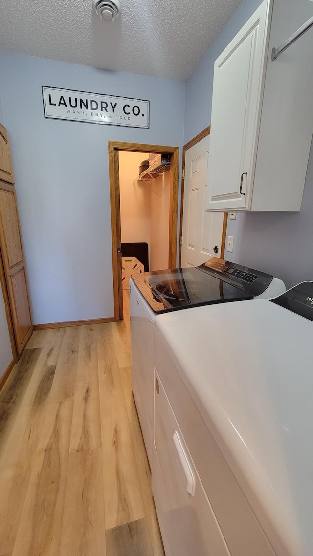 clothes washing area with light wood-style floors, a textured ceiling, cabinet space, and washer and clothes dryer