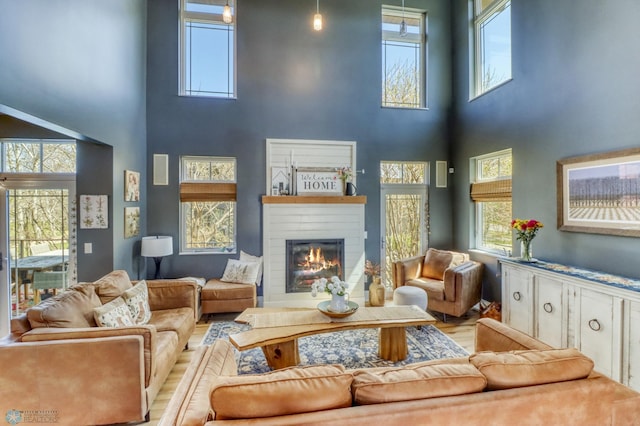 living room with a glass covered fireplace, wood finished floors, and a towering ceiling
