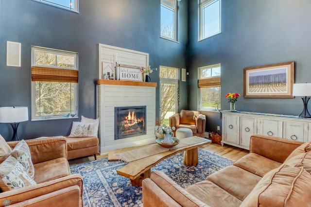 living room with a high ceiling, a glass covered fireplace, and wood finished floors