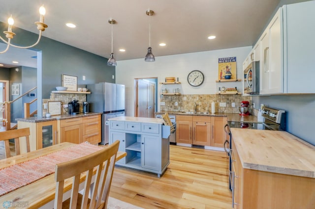 kitchen with decorative backsplash, open shelves, a sink, light wood finished floors, and stainless steel appliances