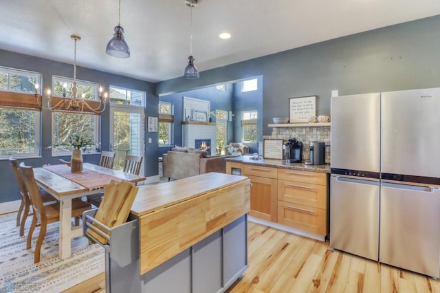 kitchen with a warm lit fireplace, wooden counters, light wood-style flooring, freestanding refrigerator, and recessed lighting