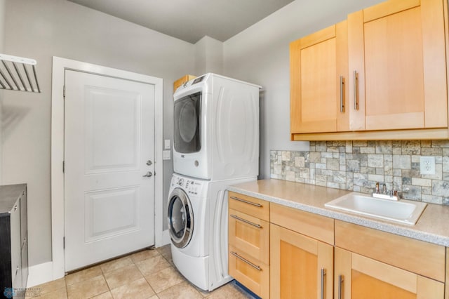 laundry room with a sink, cabinet space, light tile patterned flooring, and stacked washer / dryer