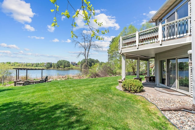 view of grassy yard with a water view, a balcony, and a patio area