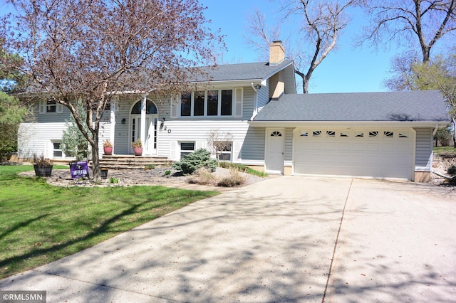 split foyer home featuring roof with shingles, an attached garage, concrete driveway, a front yard, and a chimney