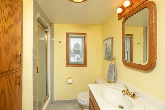 full bath featuring vanity, tile patterned floors, baseboards, toilet, and a shower with door