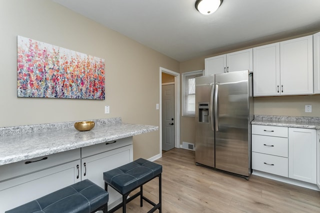 kitchen with light countertops, stainless steel fridge with ice dispenser, light wood finished floors, and white cabinetry