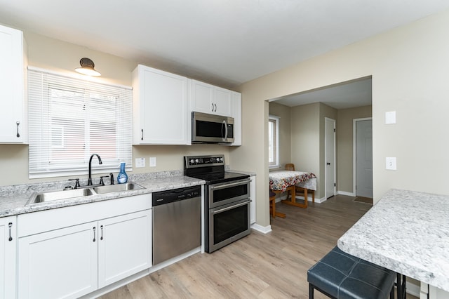 kitchen with a sink, light countertops, white cabinets, light wood finished floors, and stainless steel appliances