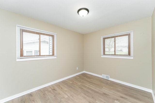 spare room with a healthy amount of sunlight, baseboards, light wood finished floors, and visible vents