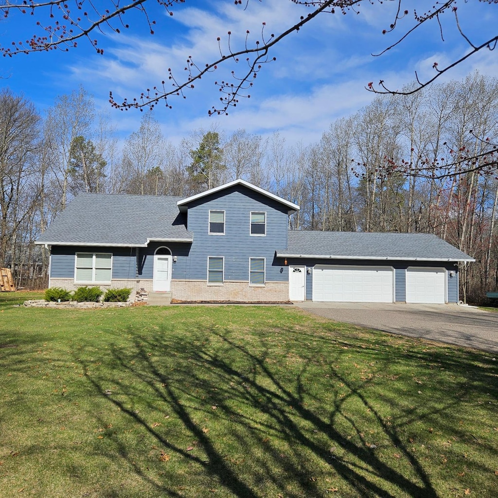 tri-level home with a garage, a shingled roof, a front lawn, and aphalt driveway