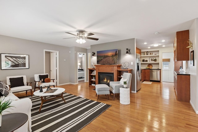 living area featuring a ceiling fan, baseboards, a glass covered fireplace, recessed lighting, and light wood-style flooring