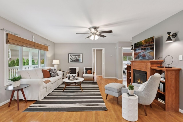 living area featuring a glass covered fireplace, baseboards, ceiling fan, and wood finished floors